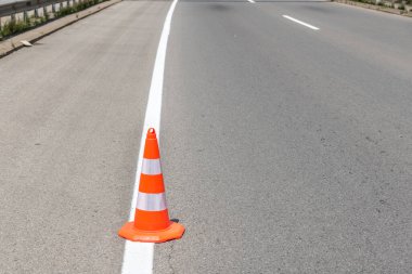 Sokaktaki turuncu trafik konisi bariyeri asfalt yolu ayrımında taze beyaz boya lekelerini korur.