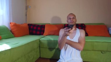 Genç, sıska, kel bir adam evinde oturmuş sıkılmış ve depresyonda. Zamanını televizyon programlarını ya da kanalları değiştirerek geçiriyor. TV kumandalı, komik adam konseptiyle.