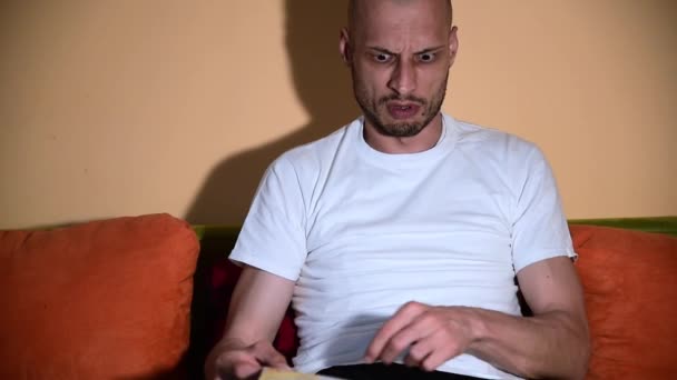 Hombre Haciendo Expresiones Faciales Divertidas Mientras Navega Revista Para Adultos — Vídeo de stock
