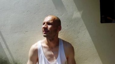 Genç, sıska, iştah açıcı uyuşturucu bağımlısı ve akıl hastası evsiz bir adam sıcak bir yaz gününde sokakta oturuyor ve taze su içmek için alnından ve başından ter süzülüyor.