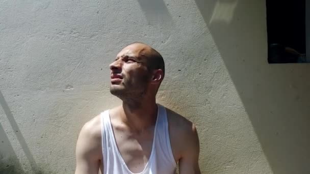 暑い夏の日に街の通りに座っている若いスキニー拒食症の麻薬中毒者と精神疾患のホームレスの男は 頭と額から汗を拭き取ります喉の渇き水のためにリフレッシュする — ストック動画
