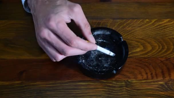 在木制桌子或酒吧上方的黑色陶瓷烟灰缸里抽烟的男性烟民手 — 图库视频影像
