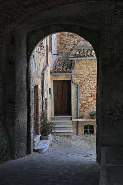 Narrow street of medieval italian town Montemerano with arch, door and cobblestone, Italy