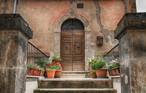 Old wooden door decorated with flowerpots and steps from the medieval town, Tuscany, Italy
