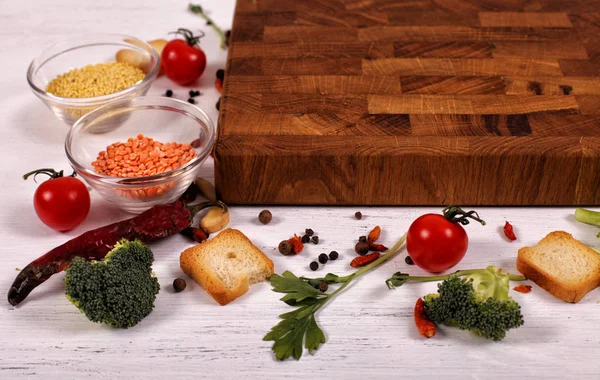 Økologisk mat med tom, brun nedskjæringsplate på hvitt trebord – stockfoto