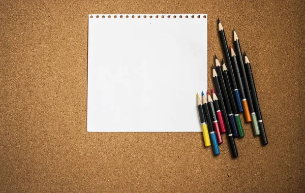 软木塞背景上的白纸和彩色铅笔 — 图库照片