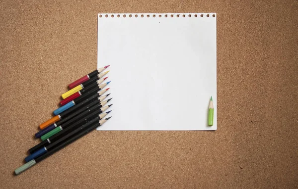 Varios lápices de colores sobre corcho Fondo del tablero con shee blanco — Foto de Stock