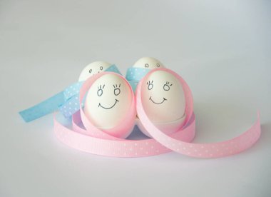 Mavi ve pembe kurdelelere sarılı gülümseyen iki beyaz yumurta, beyaz arka planda. Mutlu Paskalyalar. Yeni hayat konsepti. Tatil kartı. 