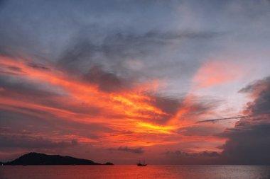 Ateşli bir günbatımı gökyüzünün arka planına karşı denizde bir gemi. Tayland.