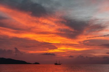 Ateşli bir günbatımı gökyüzünün arka planına karşı denizde bir gemi. Tayland.