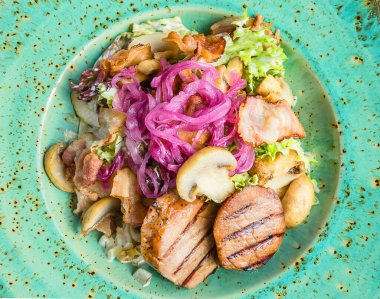Domuz etli ızgara salata: salata, pastırma, soğan turşusu, mantar, turkuaz tabakta tartar sosu. Kapat.