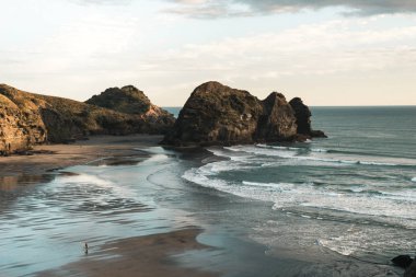 Kaya oluşumları Yeni Zelanda Piha sahil plaj, altın gün batımı, ışık dalgaları geliyor beach.