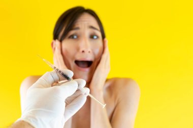 Genç bir kadın korku içinde şırıngaya bakıyor ve bağırıyor (elinde şırıngayla eline odaklanıyor) - güzellik enjeksiyonu, kozmetoloji ve güzellik tedavileri, invazif profesyonel cilt bakımı kavramı