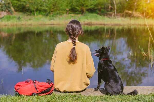 犬と屋外に座って湖を見ている女の子の後部ビュー 友情と旅行のコンセプト — ストック写真