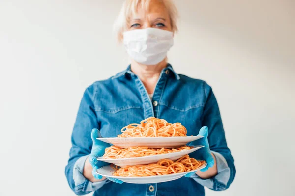 Portrait of waitress holding plates of Italian spaghetti pasta wearing protective surgical mask and latex gloves - concept of food delivery restaurants (fast food) during or after coronavirus epidemic