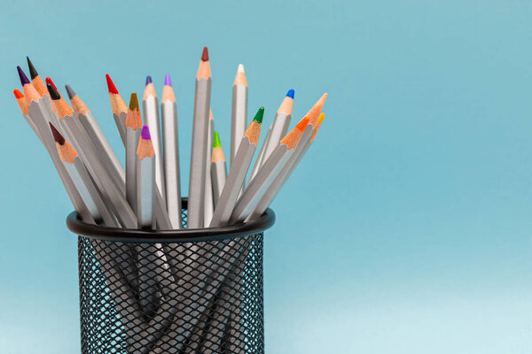 gray wooden pencils with colored rods in the stand on a blue background