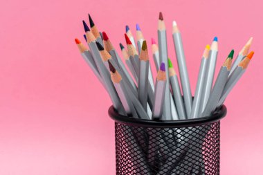 Gül arka planında renkli çubukları olan gri tahta kalemler.