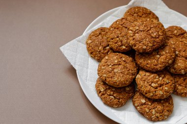 Kahverengi arka planda beyaz tabakta yulaflı kurabiyeler.