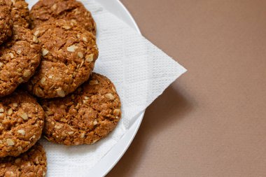 Kahverengi arka planda beyaz tabakta yulaflı kurabiyeler.