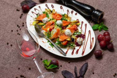 Somonlu taze salata, avokado, büyük beyaz tabakta peynir ve tekstil kakao rengi arka planda bir bardak kırmızı şarap.