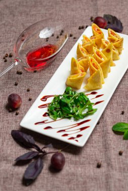 Havyar ve roka ile birlikte beyaz tabakta soslu dilimlenmiş gözleme, bir bardak kırmızı şarap, kahve arka planında beyaz bir tabakta sos.