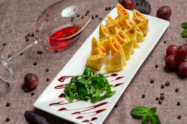 Havyar ve roka ile birlikte beyaz tabakta soslu dilimlenmiş gözleme, bir bardak kırmızı şarap, kahve arka planında beyaz bir tabakta sos.