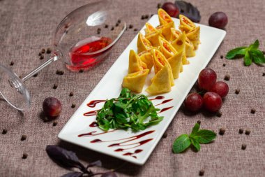 Havyar ve roka ile birlikte beyaz tabakta soslu dilimlenmiş gözleme, bir bardak kırmızı şarap, kahve arka planında beyaz bir tabakta sos.