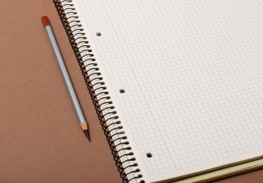 Kahverengi arkaplanda beyaz işaretli defter ve gri kalem