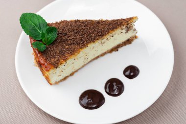 Bej bir masa örtüsünün arka planında beyaz bir tabakta nane yapraklı bir parça cheesecake.