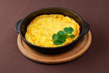 Siyah dökme demir bir pandanın içindeki yumurtalardan omlet, otlar, maydanoz.