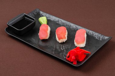 Somon, zencefil, wasabi, siyah tabakta soya soslu suşi, kahverengi tekstil arka planına yakın.