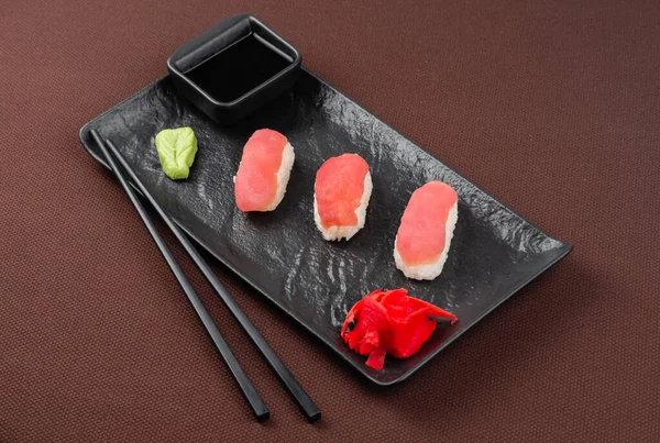 带有鲑鱼 酱油和筷子的寿司生鱼片放在褐色纺织品背景的黑盘上 — 图库照片