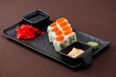 Somonlu suşi, ton balığı, pirinç, zencefil, soya sosu siyah bir tabakta kahverengi bir tekstil arka planında.