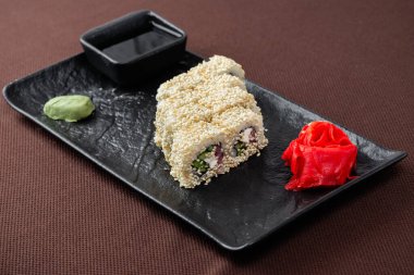 Somonlu suşi, ton balığı, pirinç, zencefil, soya sosu siyah bir tabakta kahverengi bir tekstil arka planında.