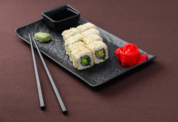 sushi with salmon, tuna, rice, ginger, soy sauce and chopsticks for sushi on a black plate close up on a brown textile background