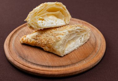 Kahverengi arka planda tahta bir tahta üzerinde silan susam tohumu ve peynir dilimlenmiş Yahudi buketleri.