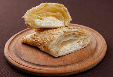 Kahverengi arka planda tahta bir tahta üzerinde silan susam tohumu ve peynir dilimlenmiş Yahudi buketleri.