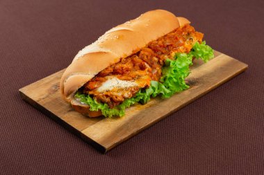 Domates soslu büyük sandviç ve kahverengi tekstil arka planında ahşap bir tahtanın üzerinde marul.