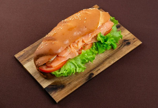 一个大三明治 上面有鲑鱼和莴苣 在一块木板上 背景是棕色的纺织品 — 图库照片