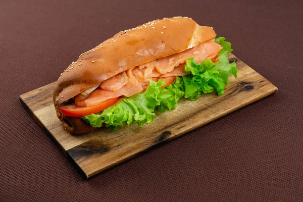 茶色の織物の背景に木の板にサーモンとレタスの大きなサンドイッチ — ストック写真