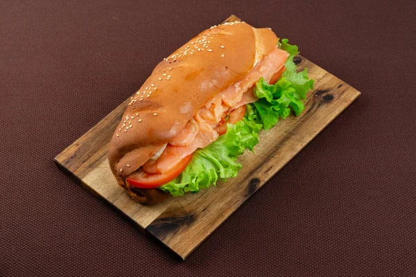 茶色の織物の背景に木の板にサーモンとレタスの大きなサンドイッチ — ストック写真