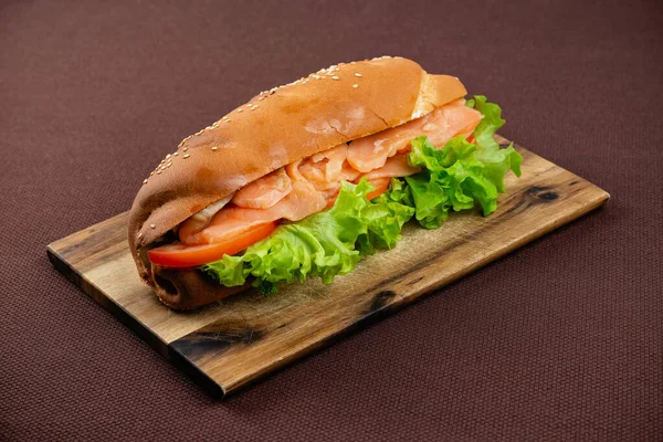 一个大三明治 上面有鲑鱼和莴苣 在一块木板上 背景是棕色的纺织品 — 图库照片