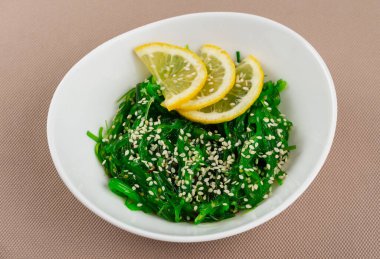 Seaweed Chuka salatası, susamlı ve limonlu bej kumaş arka planında beyaz bir tabakta.