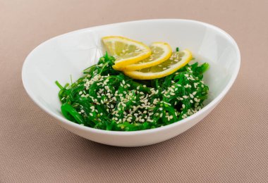 Seaweed Chuka salatası, susamlı ve limonlu bej kumaş arka planında beyaz bir tabakta.