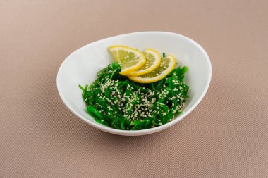 Seaweed Chuka salatası, susamlı ve limonlu bej kumaş arka planında beyaz bir tabakta.