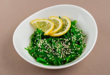 Seaweed Chuka salatası, susamlı ve limonlu bej kumaş arka planında beyaz bir tabakta.