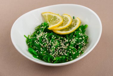 Seaweed Chuka salatası, susamlı ve limonlu bej kumaş arka planında beyaz bir tabakta.