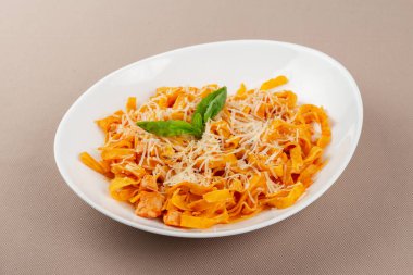 domates soslu makarna peynirli ve bej kumaş arka planında beyaz bir tabakta otlar.