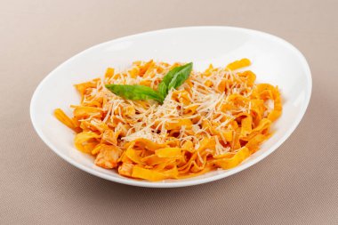 domates soslu makarna peynirli ve bej kumaş arka planında beyaz bir tabakta otlar.