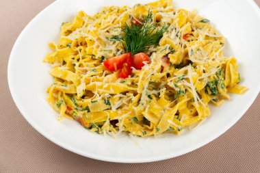 Peynirli makarna, domates, mantar ve bej kumaş arka planda beyaz bir tabakta otlar.